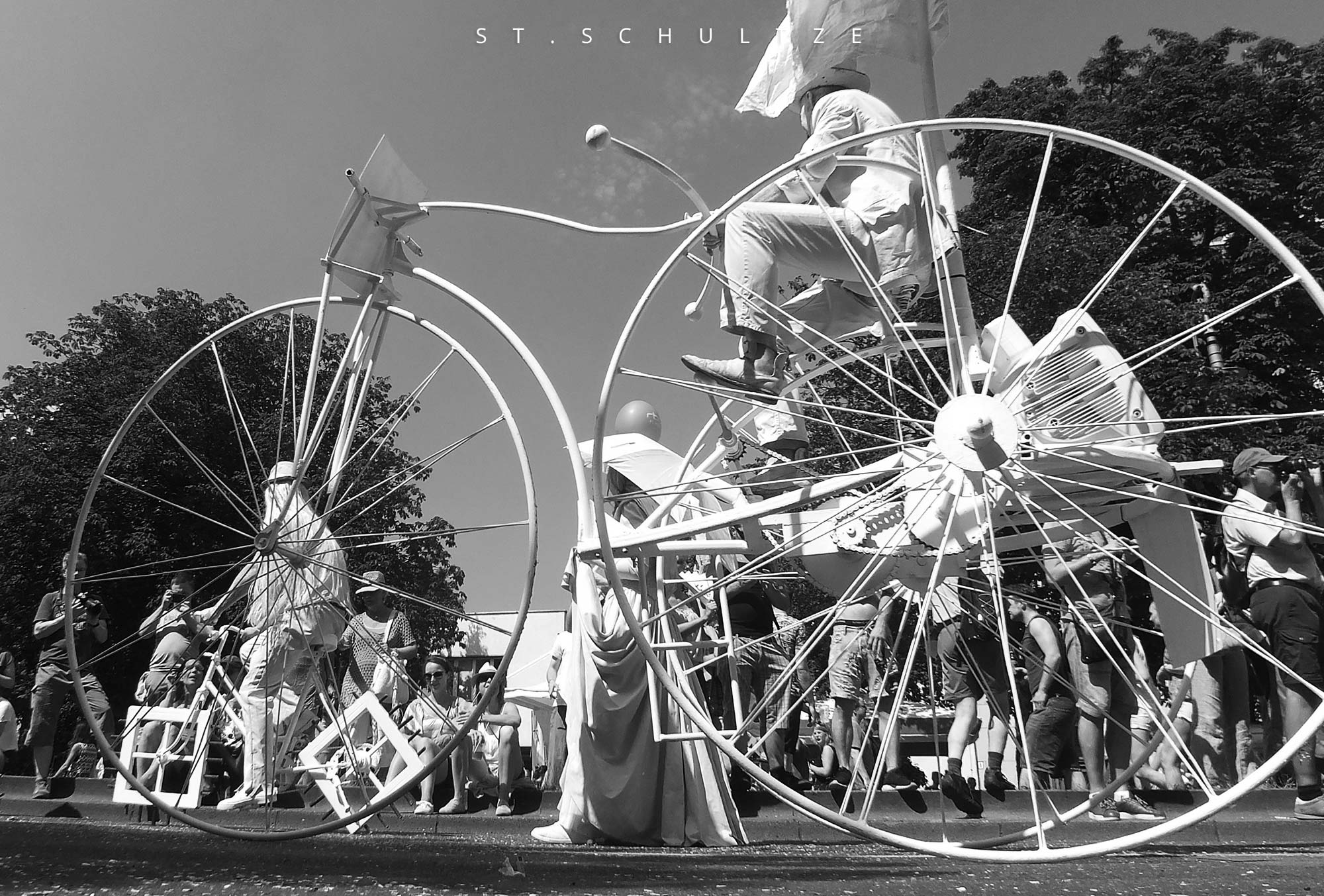 a bicycle with square wheels. a huge bicycle in the foreground - called here Riesenfahrrad - seen at the Carnical of the Cultures, Karneval der Kulturen Berlin. iconic photography, fahrrad, bicycling, radeln, showrad, sportsphotography, sportfotografie, smile